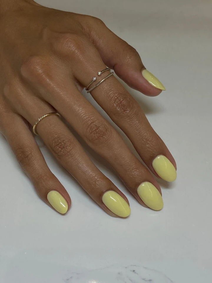 A hand model with perfectly manicured nails showcasing a creamy desaturated yellow.