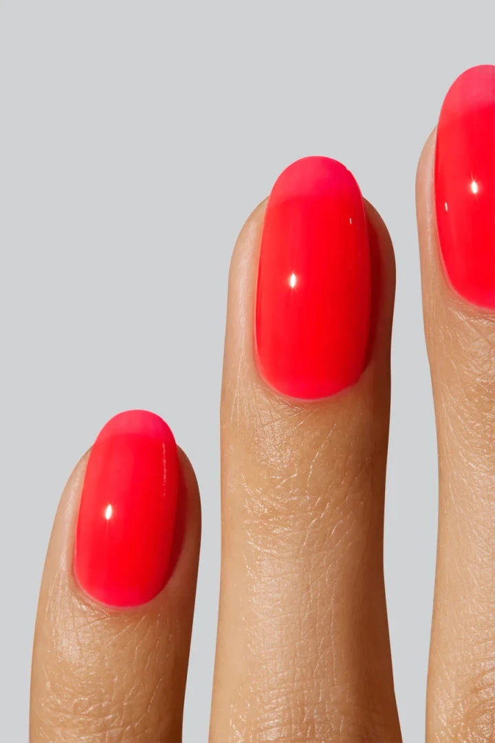 A hand model with perfectly manicured nails showcasing a juicy, jelly colour, translucent bright orange-pink.